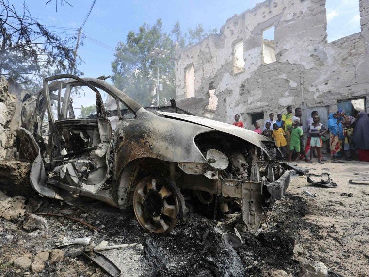 Residents gather near a destroyed car after an attack by suspected militants a national security compound in Mogadishu on August 31