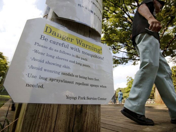 A visitor walks past a mosquitoes warning poster at Yoyogi Park in Tokyo