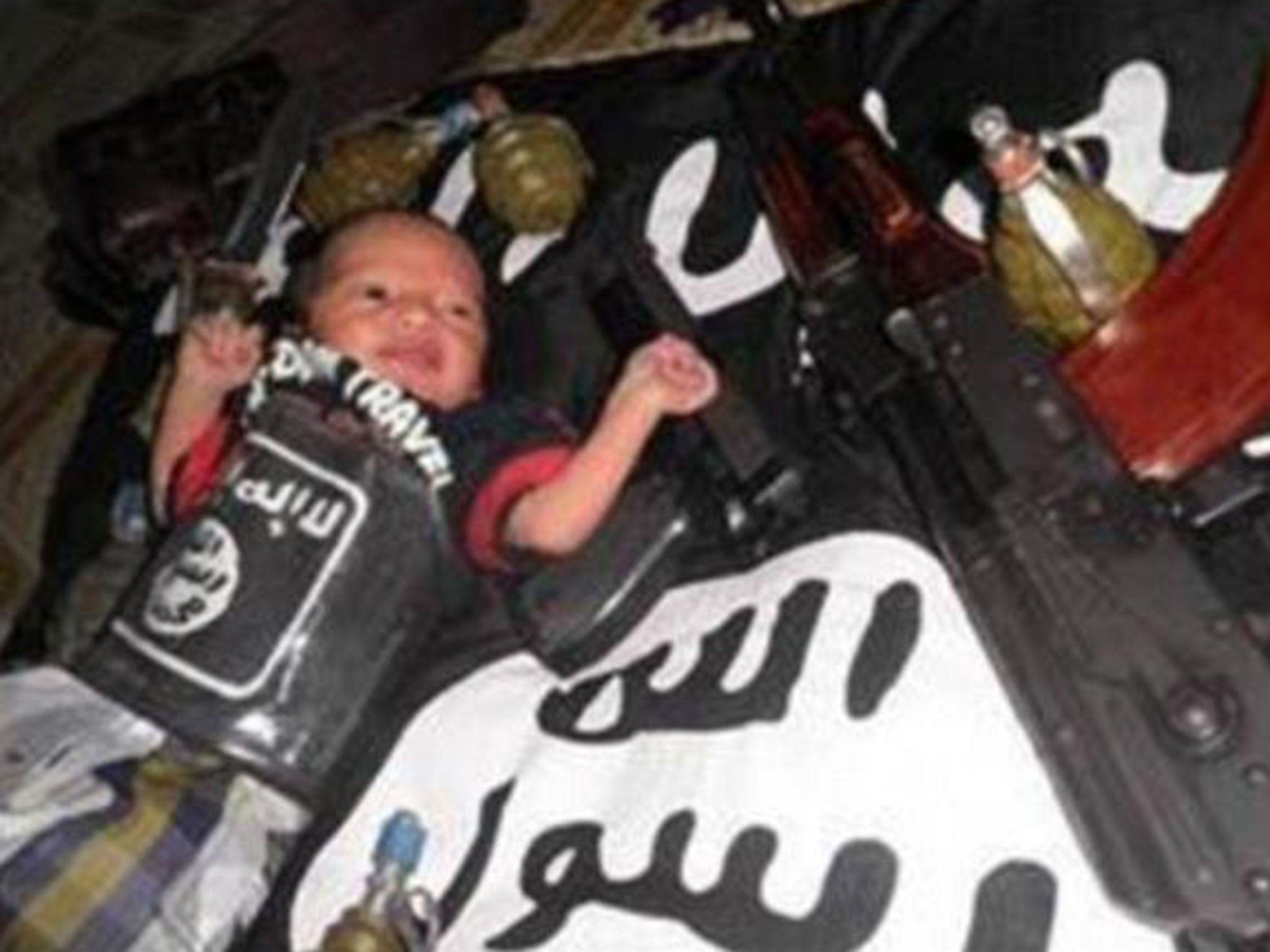 A shocking photo of a baby wrapped in an Islamic State (Isis) flag and surrounded by Kalashnikov guns is believed to have been posted online by militants