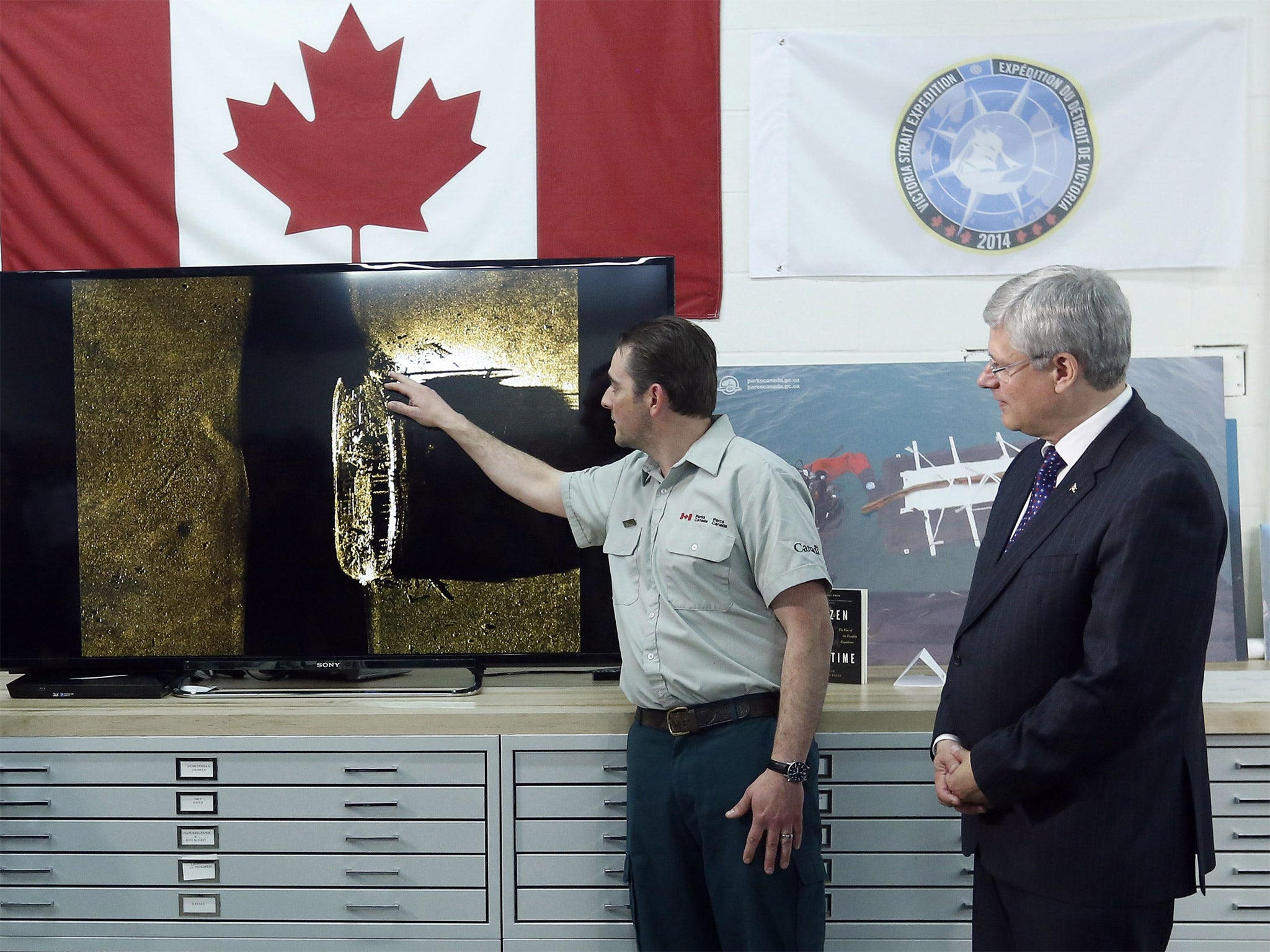 Canadian Prime Minister Stephen Harper listens as Parks Canada's Ryan Harris talks about an image showing one of two ships from the lost Franklin expedition