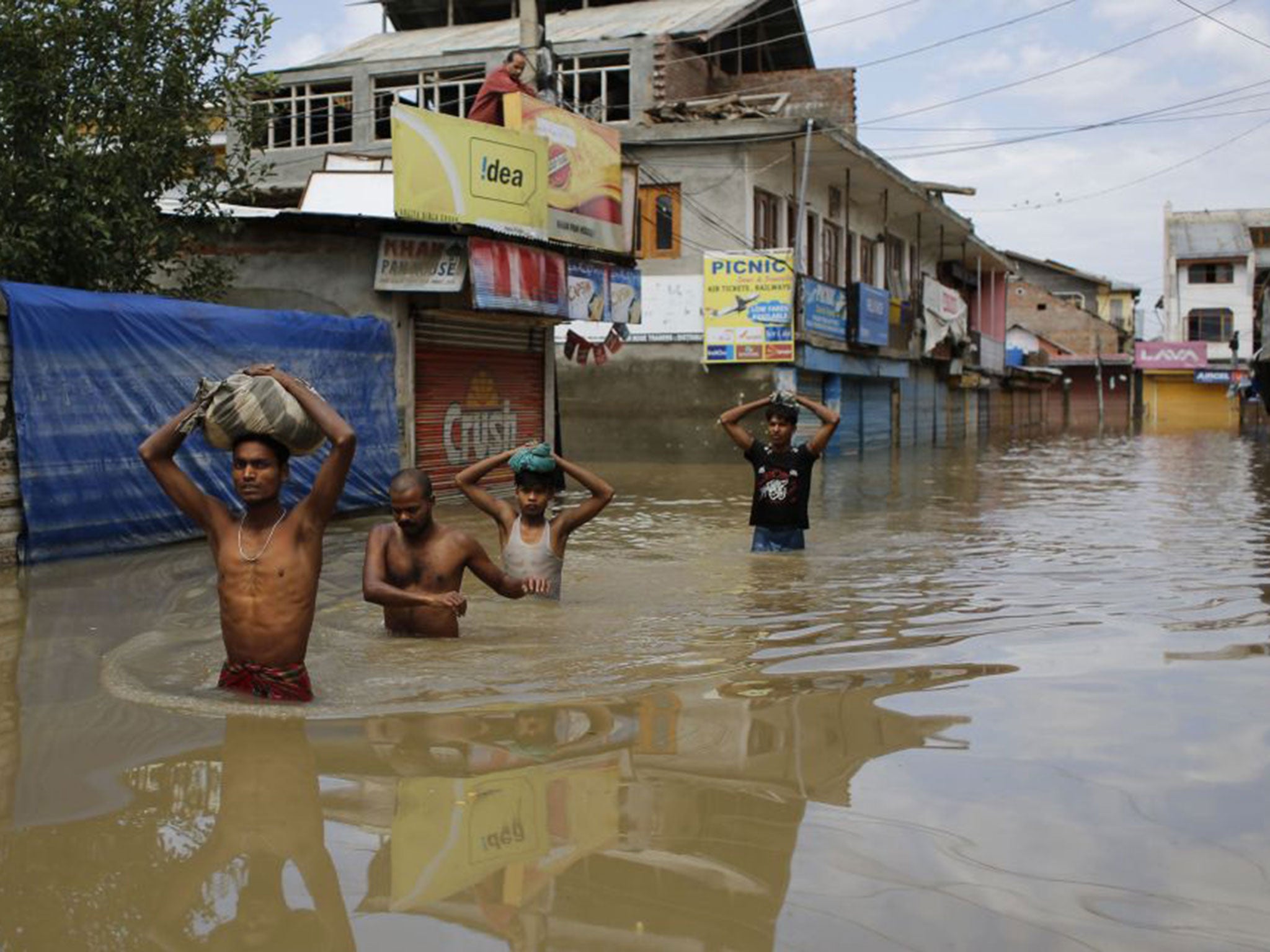 Indian migrant workers wade through receding flood waters with their belongings on their heads in Srinagar. Hundreds of people have been killed and tens of thousands are homeless
