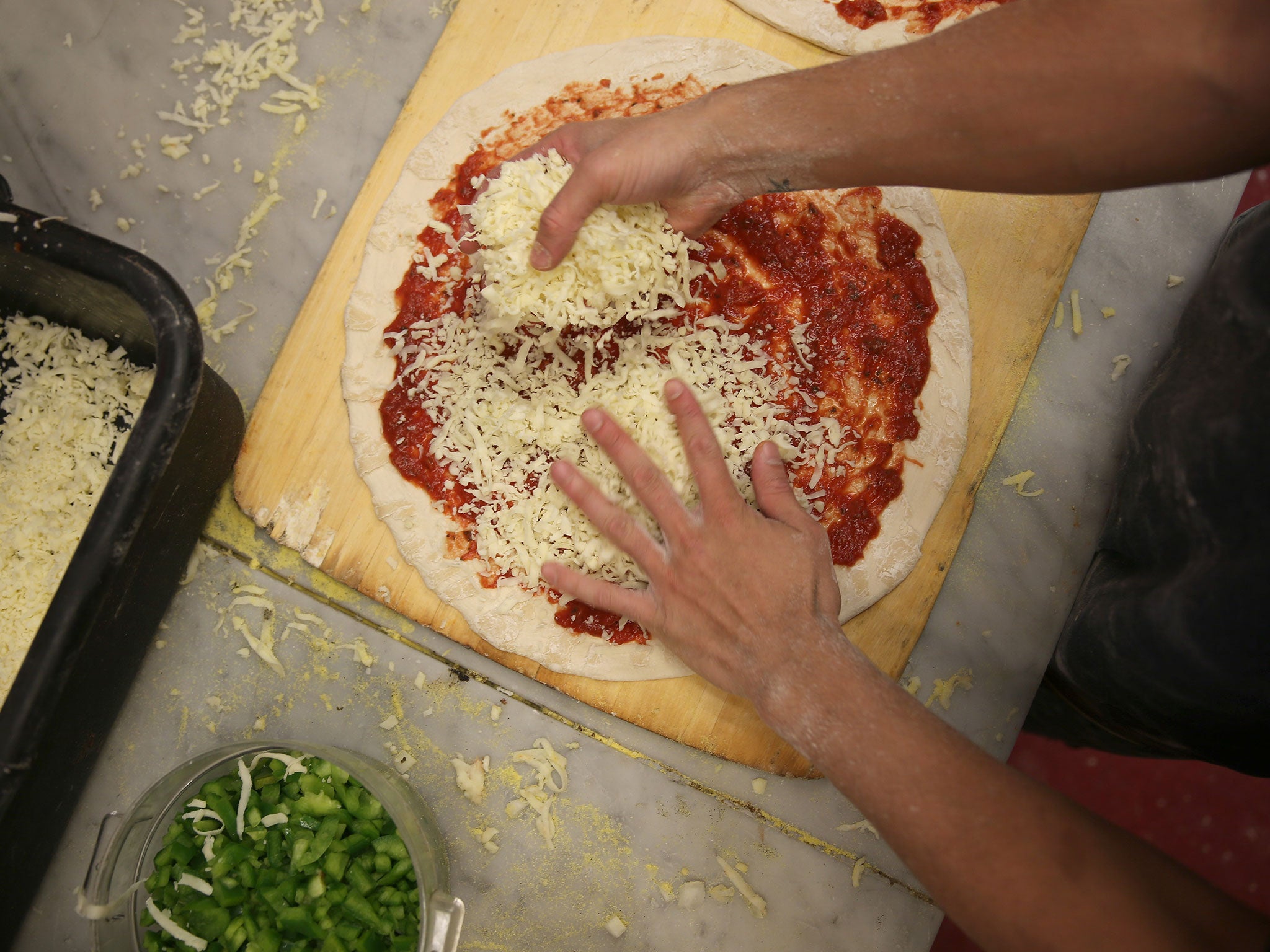 A chef sprinkles cheese onto a pizza