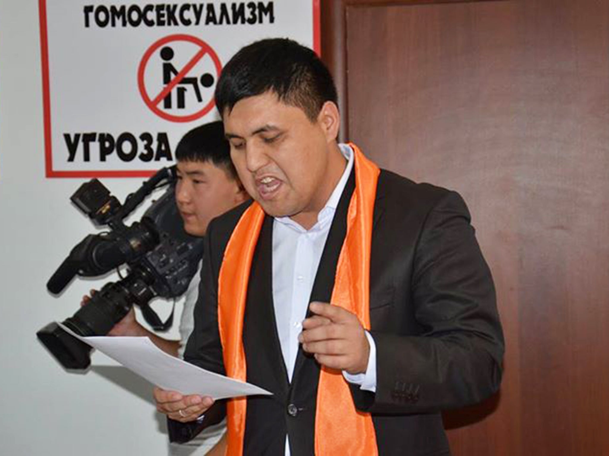 Dauren Babamuratov speaking in front of a sign reading “homosexuality is a threat to the nation"