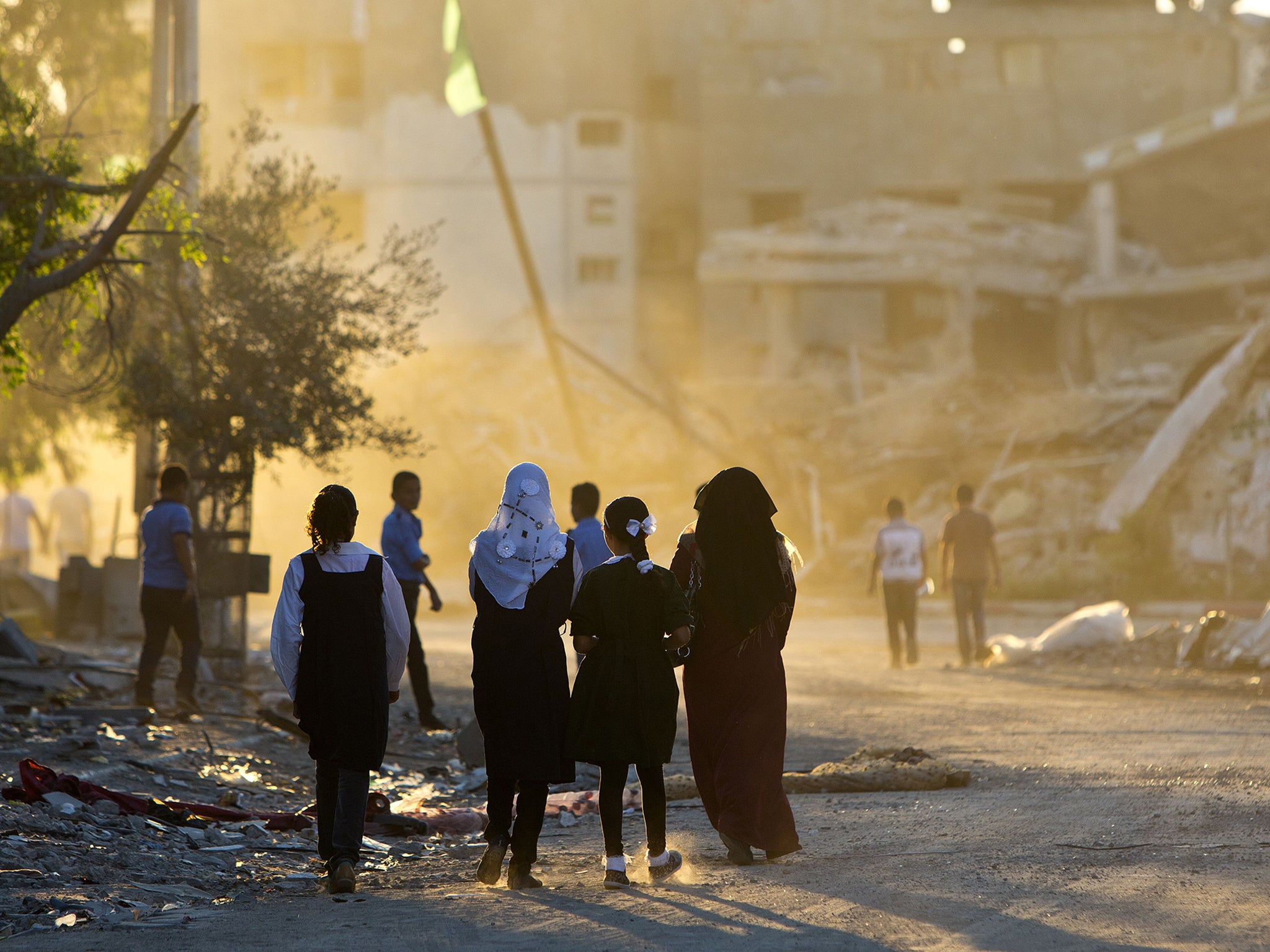 Palestinian girls walk past buildings which were destroyed by Israeli strikes on their way to school in the Shejaiya neighbourhood of Gaza City on the first day of the new school year