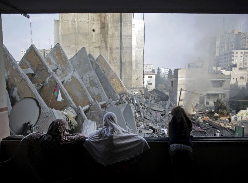 A Palestinian family looks from a window at the rubble of the collapsed 15-story Basha Tower following early morning Israeli airstrikes in Gaza City