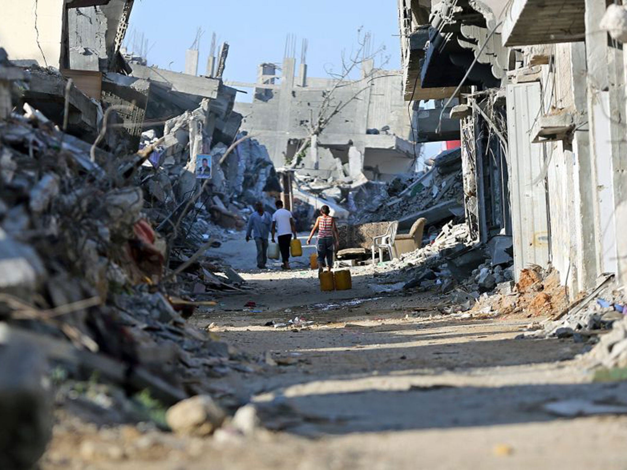 Palestinians carry plastic bottles filled with drinking water between destroyed houses (EPA)