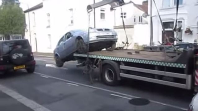 A male driver reverses his Vauxhall Astra from a tow truck