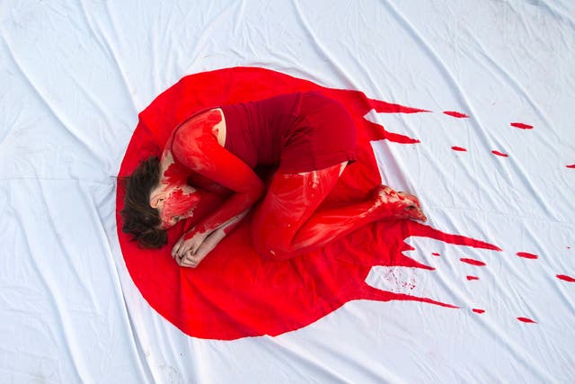 A member of the 'Taiji Dolphin Action Group' curls up on a sheet depicting the Japanese flag, during a protest against the killing of dolphins