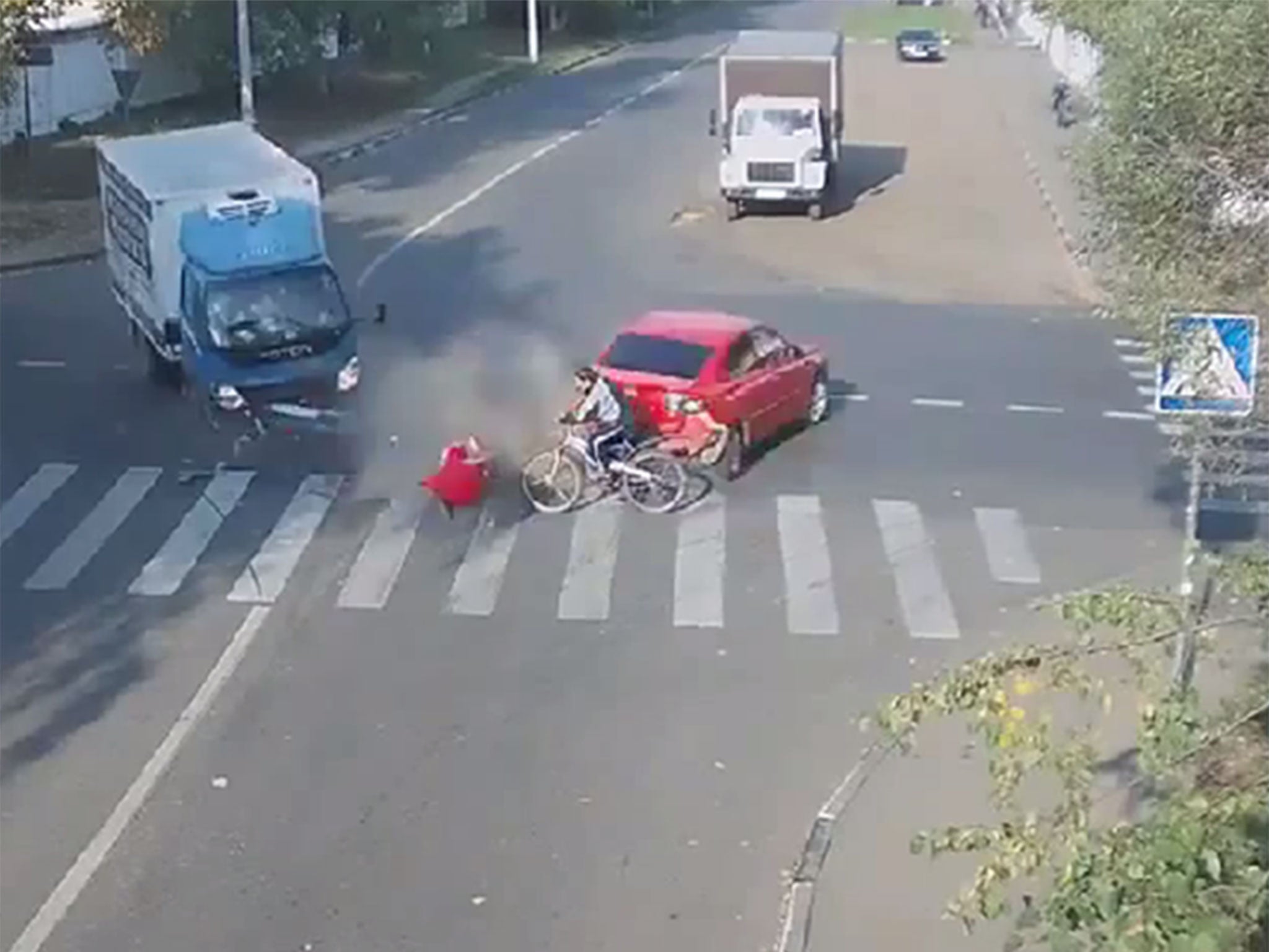 A still from a video showing a cyclist narrowly missing being hit by a car and a lorry.