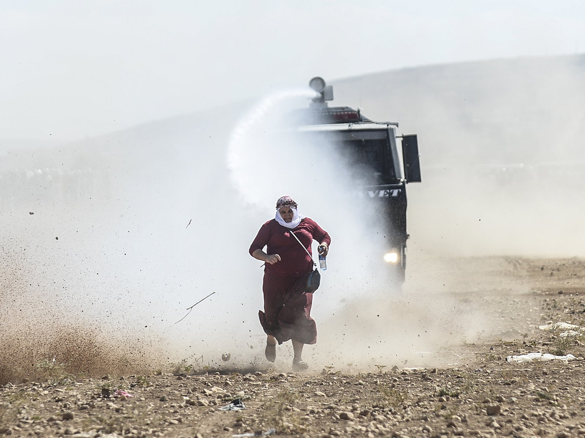 A Kurdish woman runs away from a water cannon near the Syrian border after Turkish authorities temporarily closed the border at the southeastern town of Suruc in Sanliurfa province