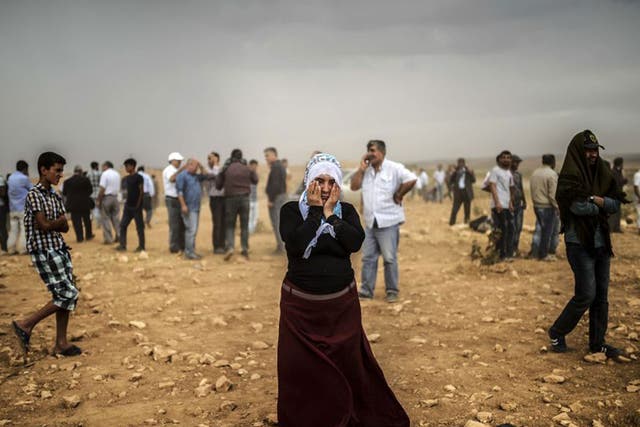 A Syrian Kurdish woman wipes her eyes during a dust storm on a hill from where people watch the battle with Isis