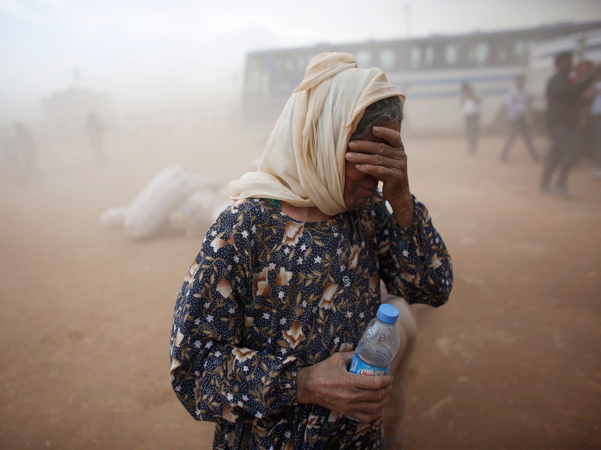 A Kurdish Syrian refugee covers her face as she waits for transport during a sand storm on the Turkish-Syrian border near the southeastern town of Suruc in Sanliurfa province
