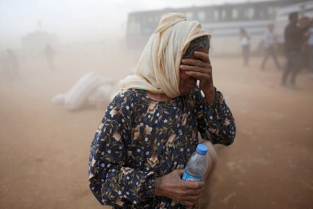 A Kurdish Syrian refugee covers her face as she waits for transport during a sand storm on the Turkish-Syrian border near the southeastern town of Suruc in Sanliurfa province  