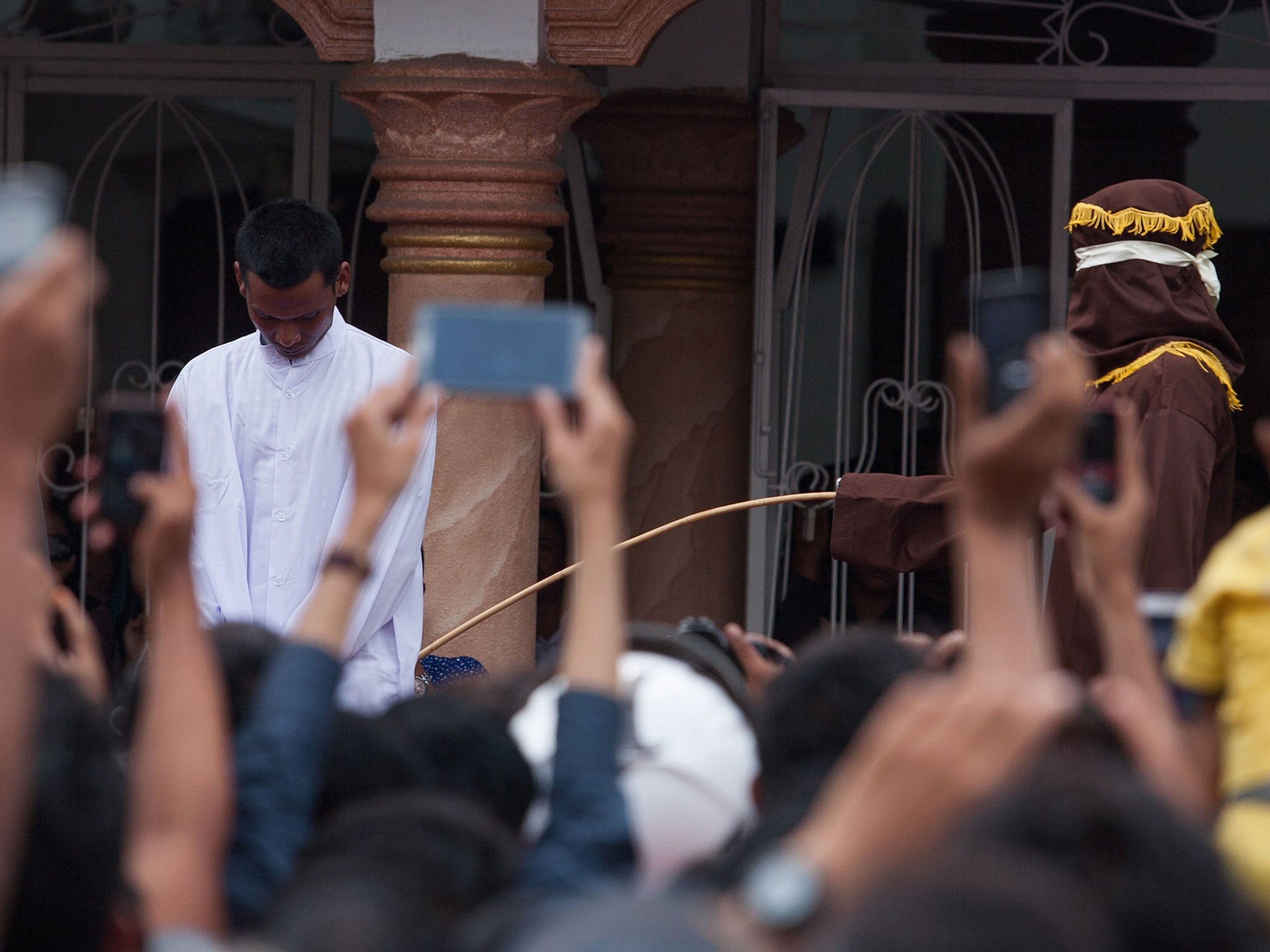 This picture taken in Banda Aceh on September 19, 2014 shows a hooded official (R, brown) caning an Aceh man for gambling in Aceh. Gay sex in Indonesia will now be punishable by the cane
