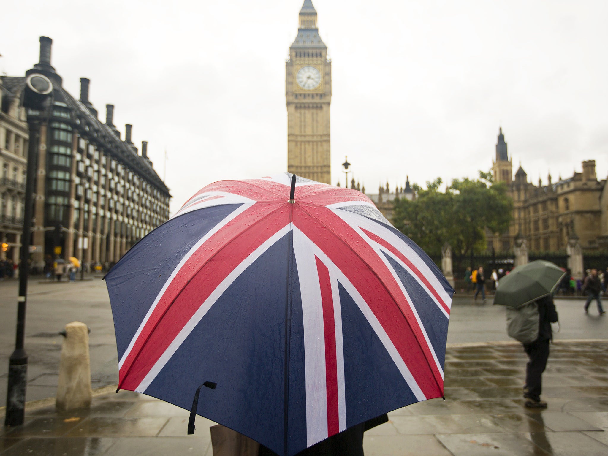 A woman shelters from the rain under an umbrella in front of the Houses of Parliament in central London