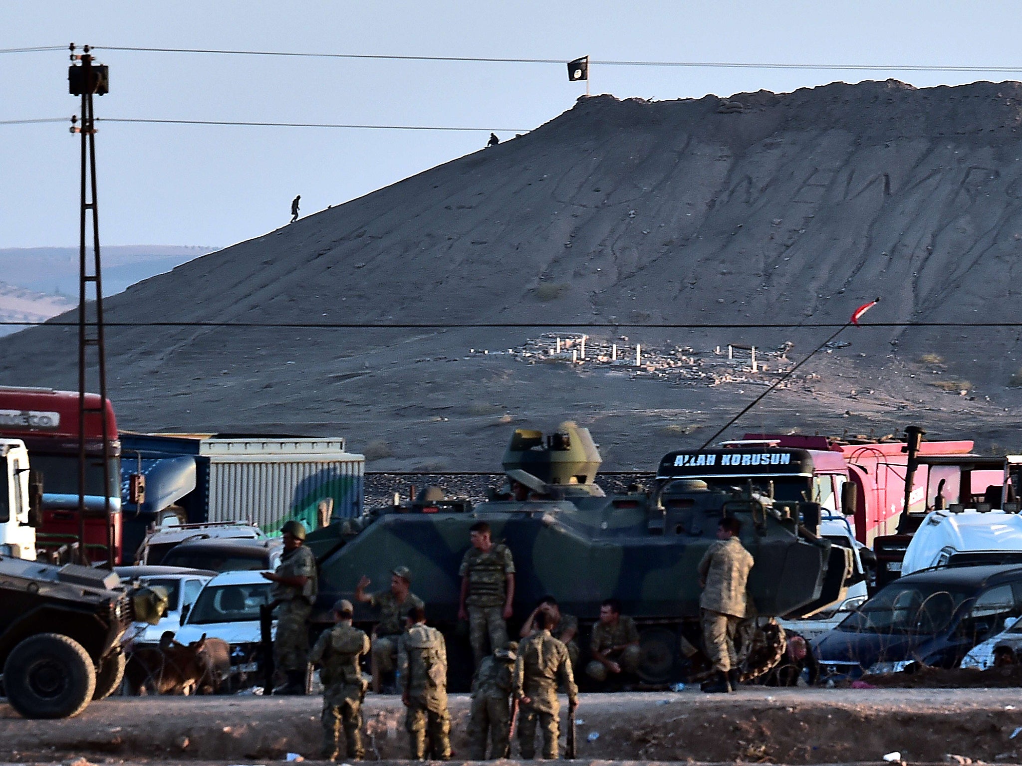 Isis militants stand next to an Isis flag atop a hill in the Syrian town of Ain al-Arab, known as Kobani by the Kurds, as seen from the Turkish-Syrian border, with Turkish troops in foreground, in the southeastern town of Suruc, Sanliurfa province