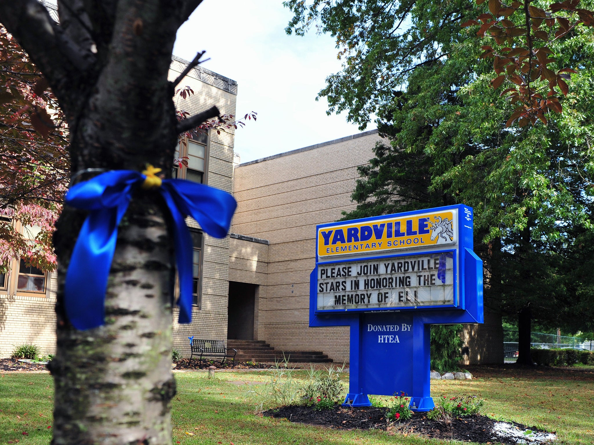 A blue and gold ribbon wrap around a tree in front of Yardville Elementary School in Hamilton Township. The ribbon and sign honored the memory of a preschooler who died on 25 September of enterovirus 68