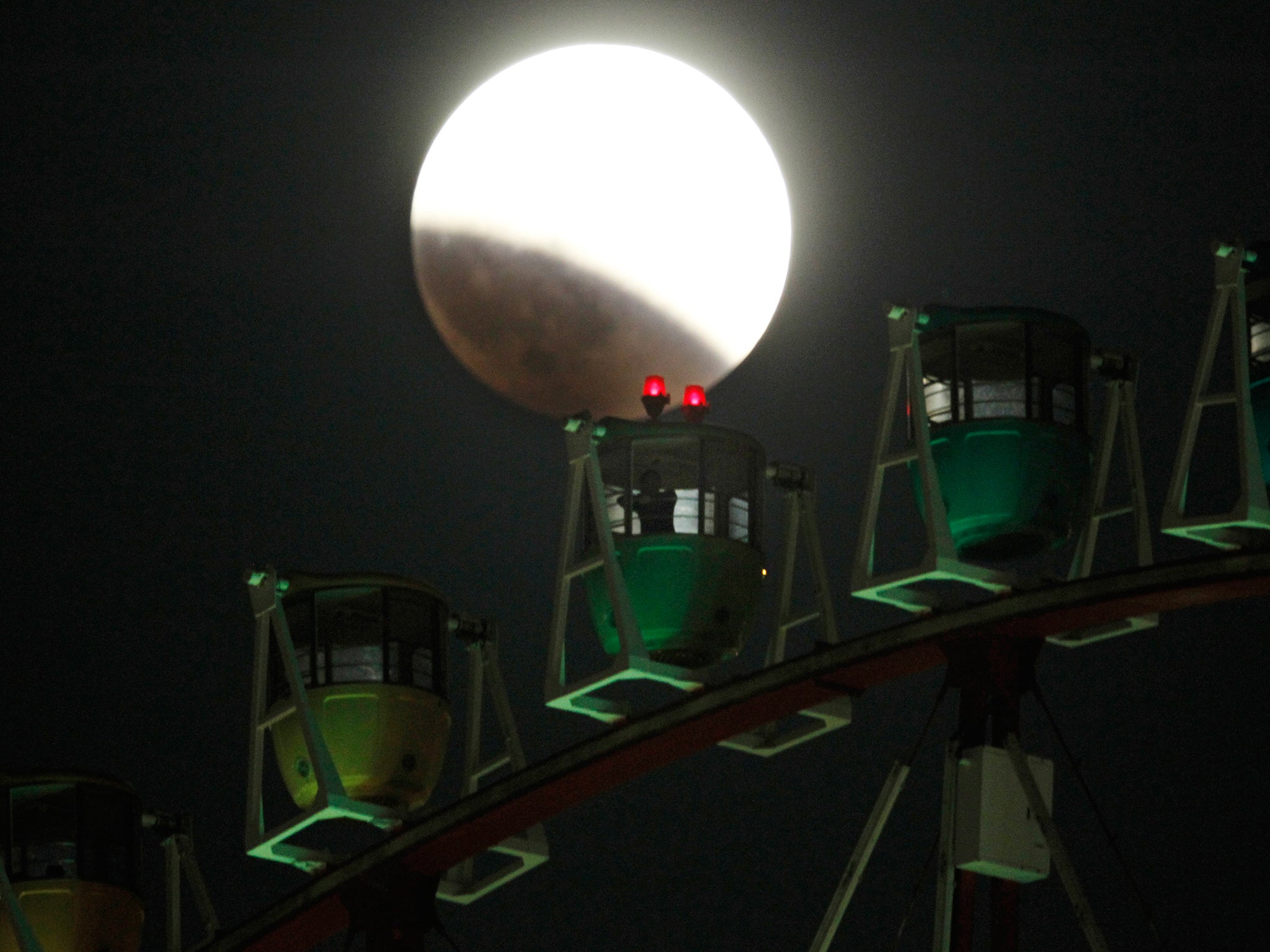The Earth's shadow renders the moon as a person in Ferris wheel observes it during a total lunar eclipse in Tokyo