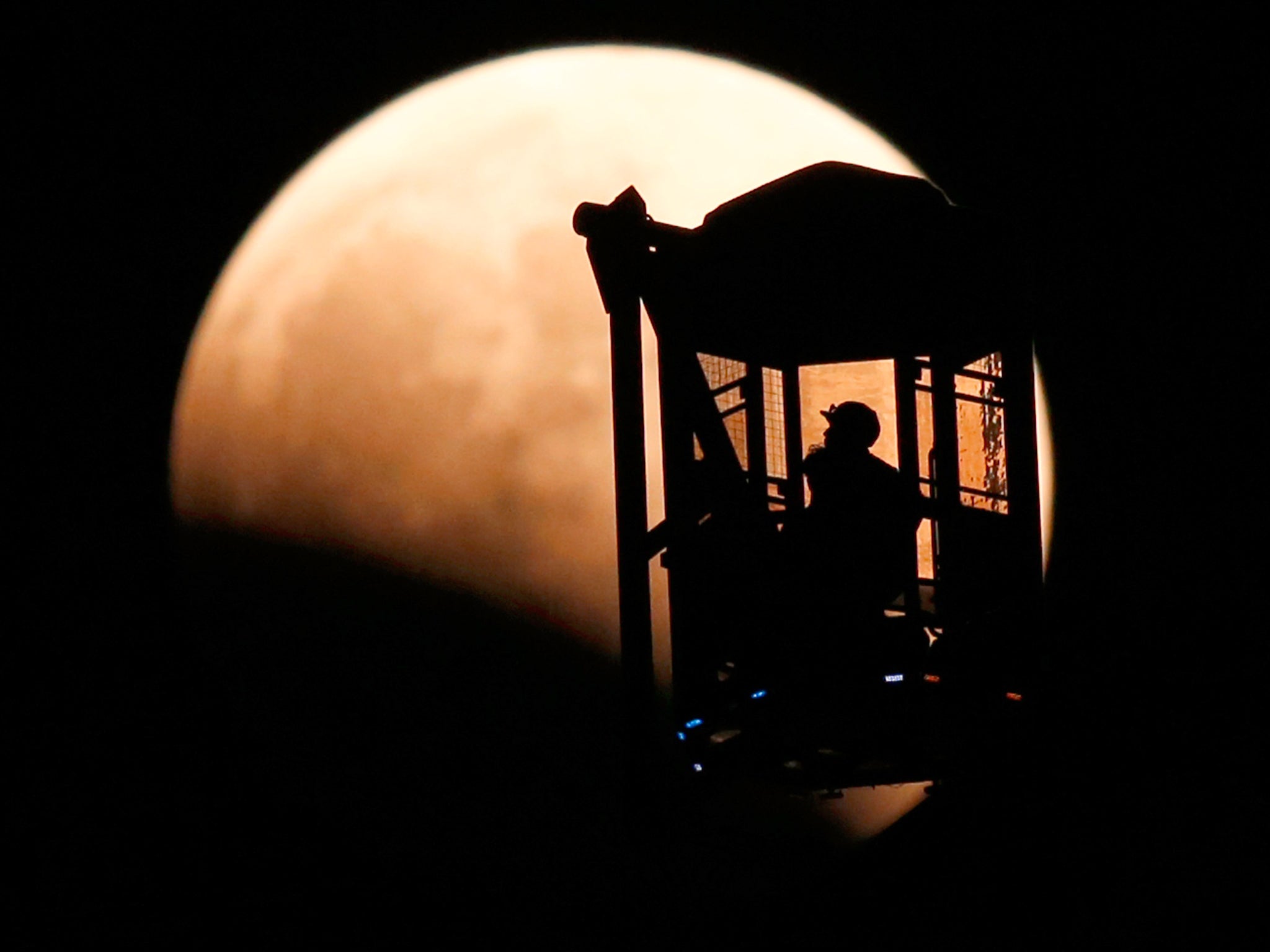 A man and a woman look at the moon as they ride a Ferris wheel, while a total lunar eclipse begins in Tokyo