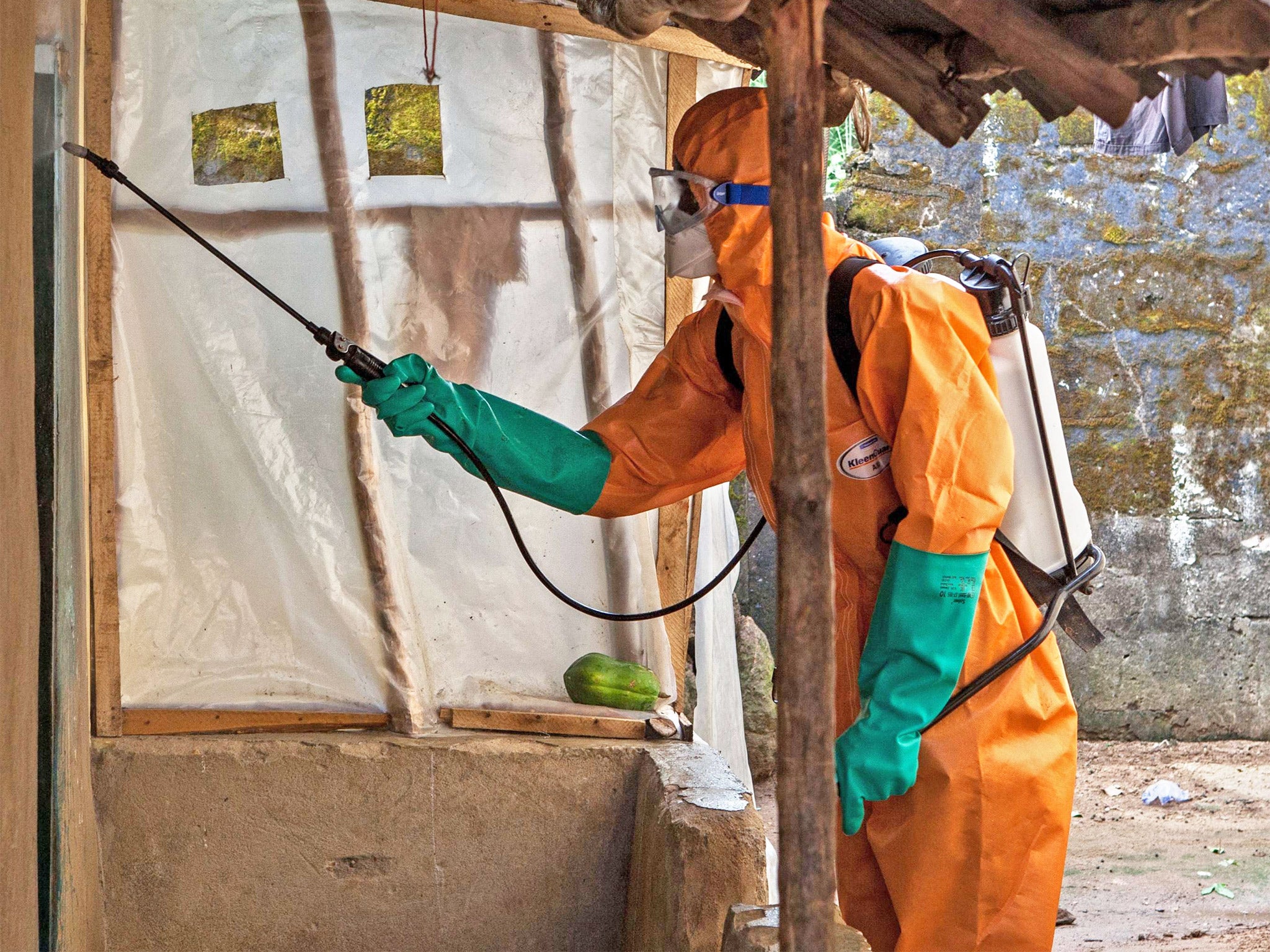 A volunteer in protective suit sprays disinfectant outside a home near Freetown, Sierra Leone