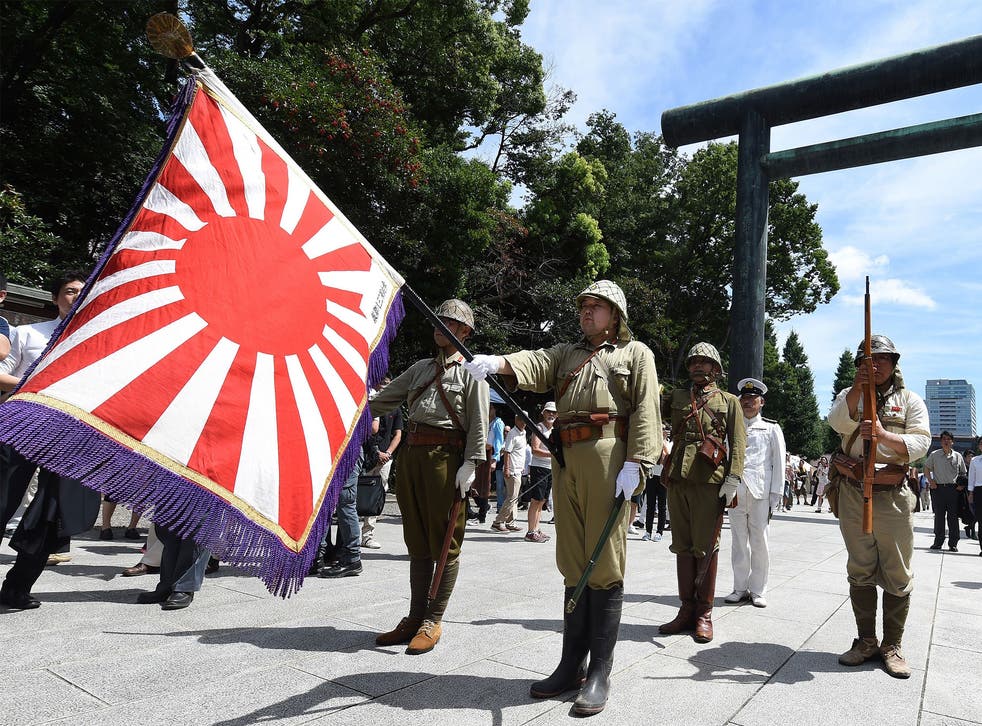 Men clad in Japanese Imperial Army and Navy uniforms stand at attention at the entrance to the controversial Yasukuni shrine as people visit to offer prayers and remember the country's war dead