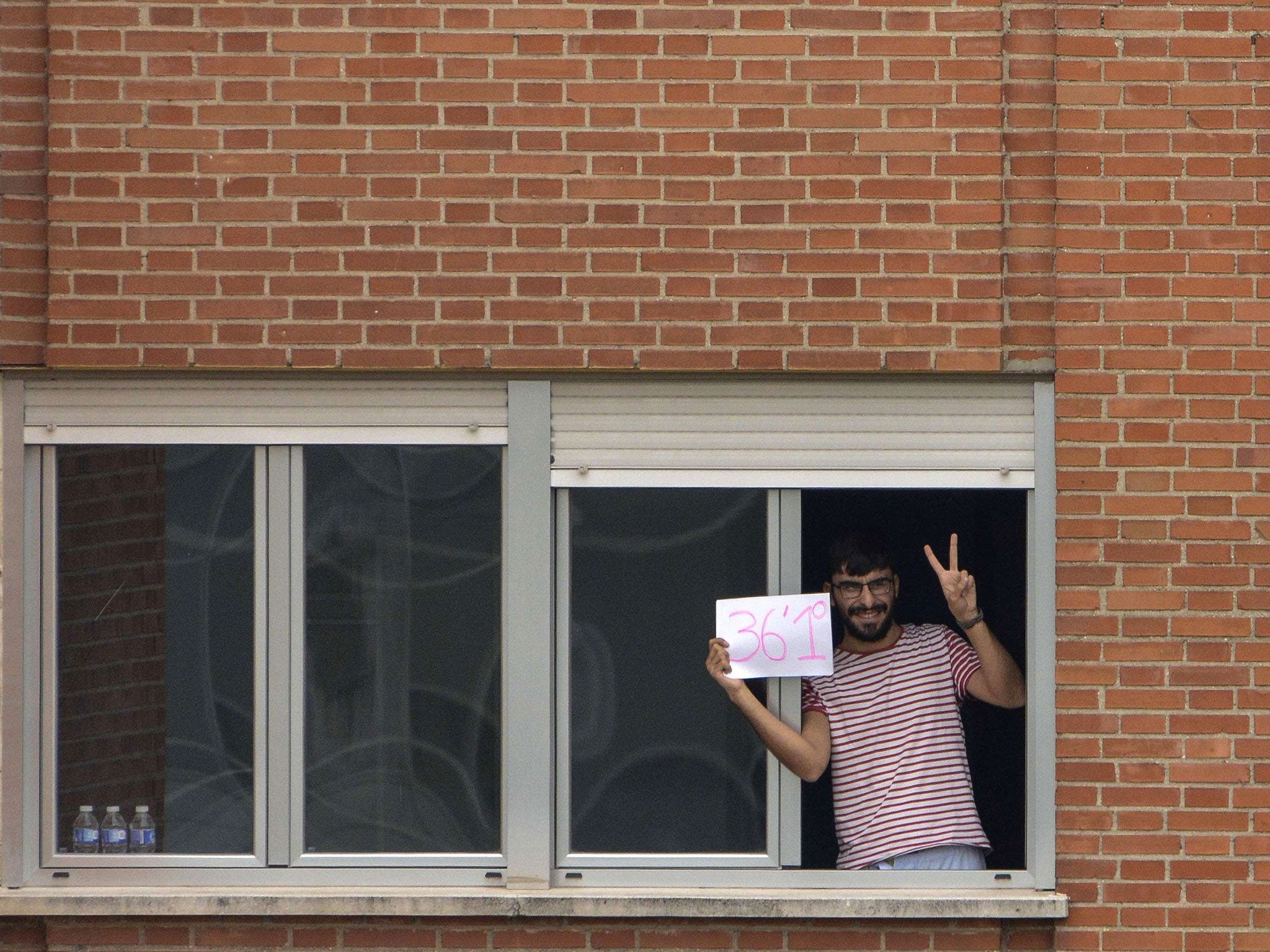 A man holds a placard with his temperature and flashes a victory sign from his window at the Carlos III hospital