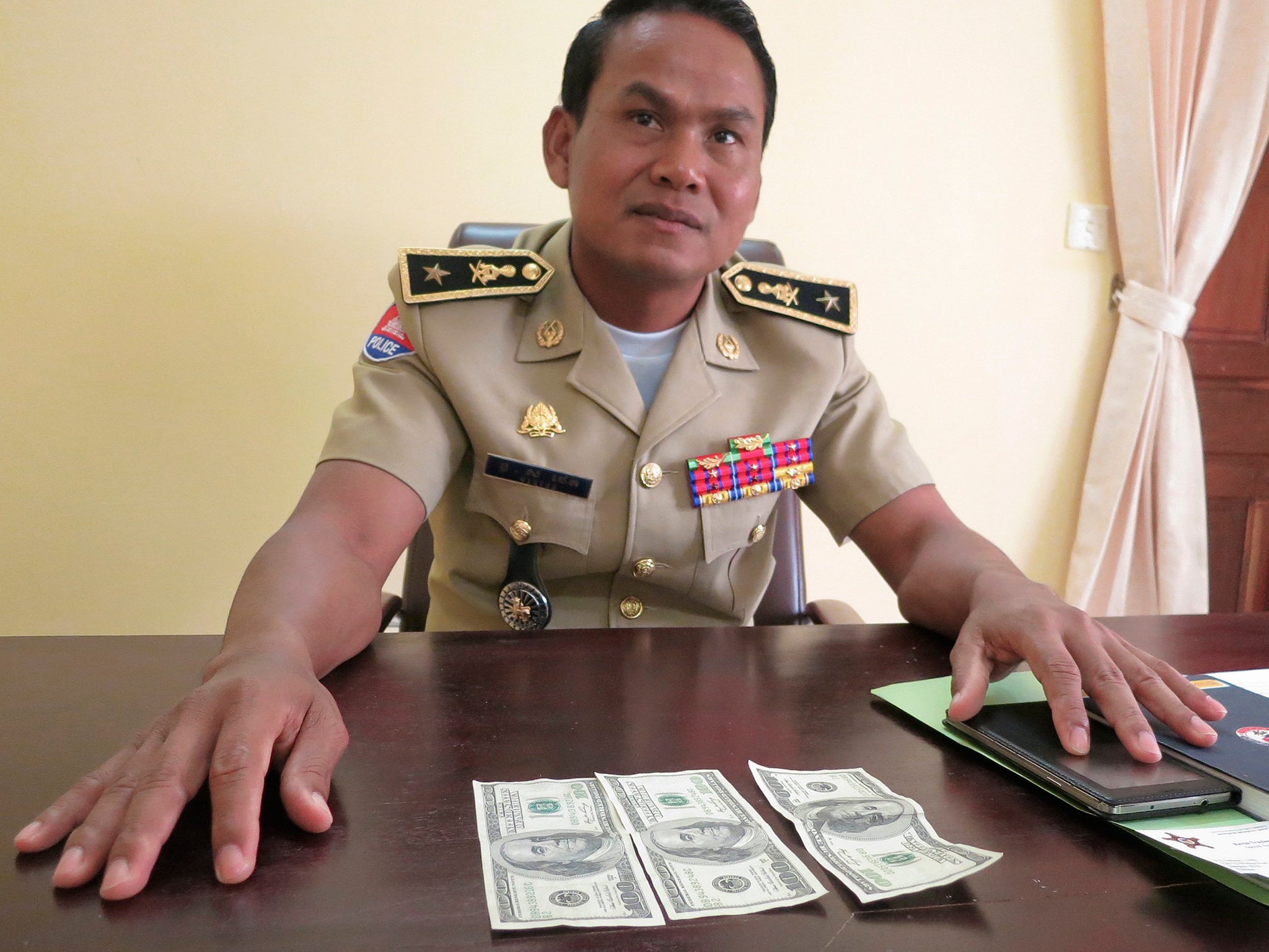 Battambang police chief Brigadier General Sar Theth poses with notes from a seized haul of $7.16 million in counterfeit hundred-dollar bills in Battambang