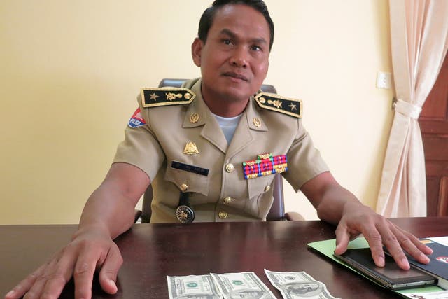 Battambang police chief Brigadier General Sar Theth poses with notes from a seized haul of $7.16 million in counterfeit hundred-dollar bills in Battambang    
