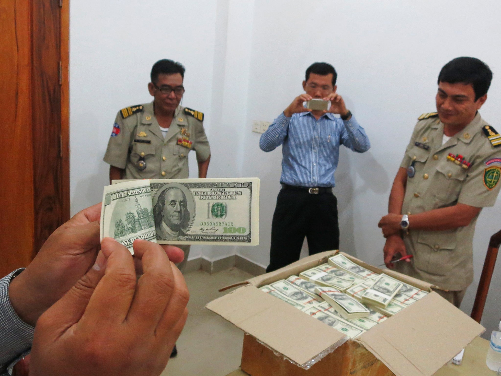 Police and court officials examine notes from a seized haul of .16 million in counterfeit hundred-dollar bills in Battambang