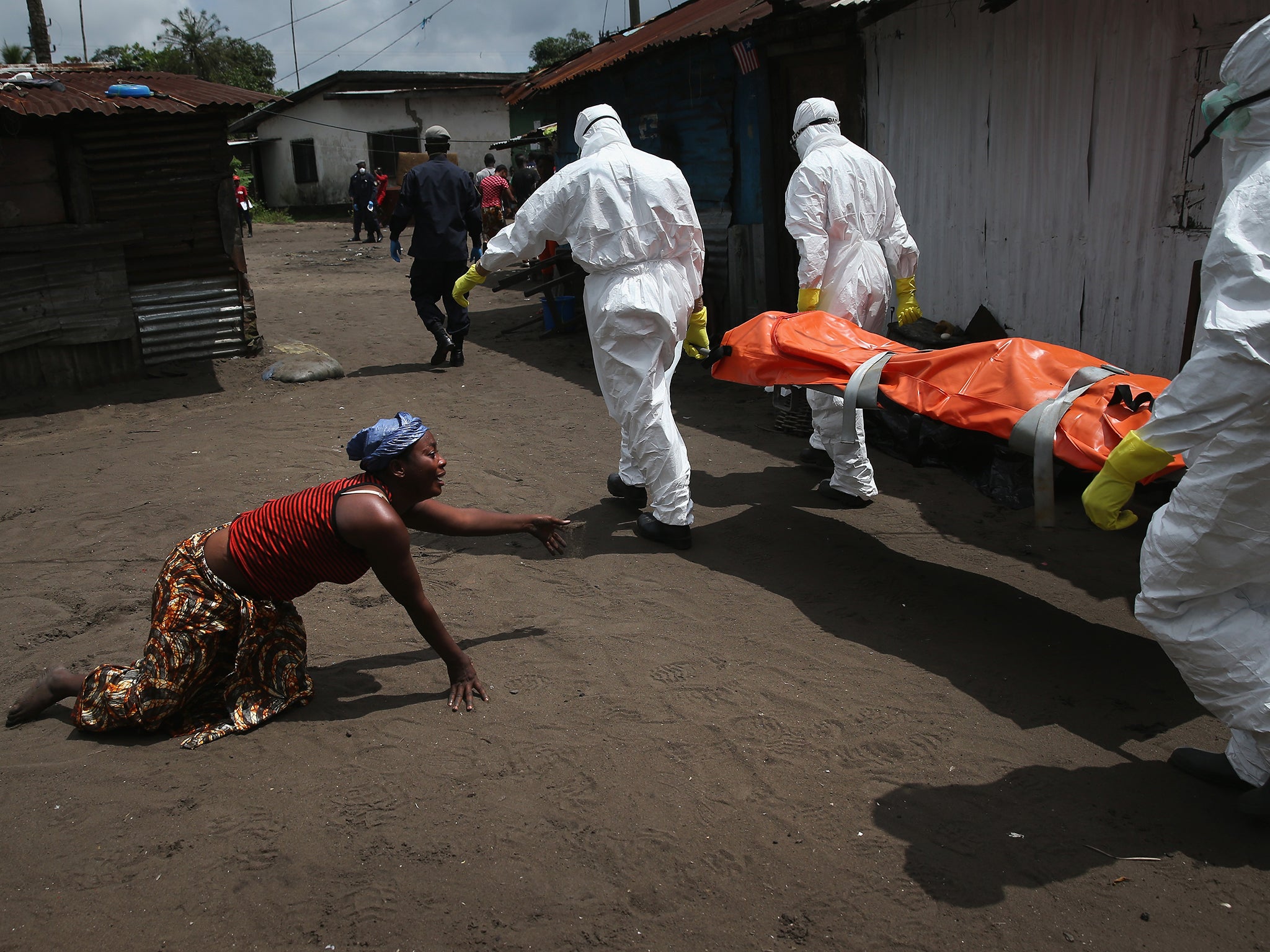 A woman crawls towards the body of her sister as Ebola burial team members take her sister Mekie Nagbe (28) for cremation in Monrovia, Liberia