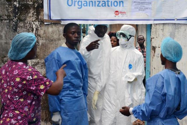 Health workers in protective gear outside the Ebola treatment unit of the John F. Kennedy Medical Center in Monrovia. Many  workers have ignored calls to strike over poor pay and working conditions