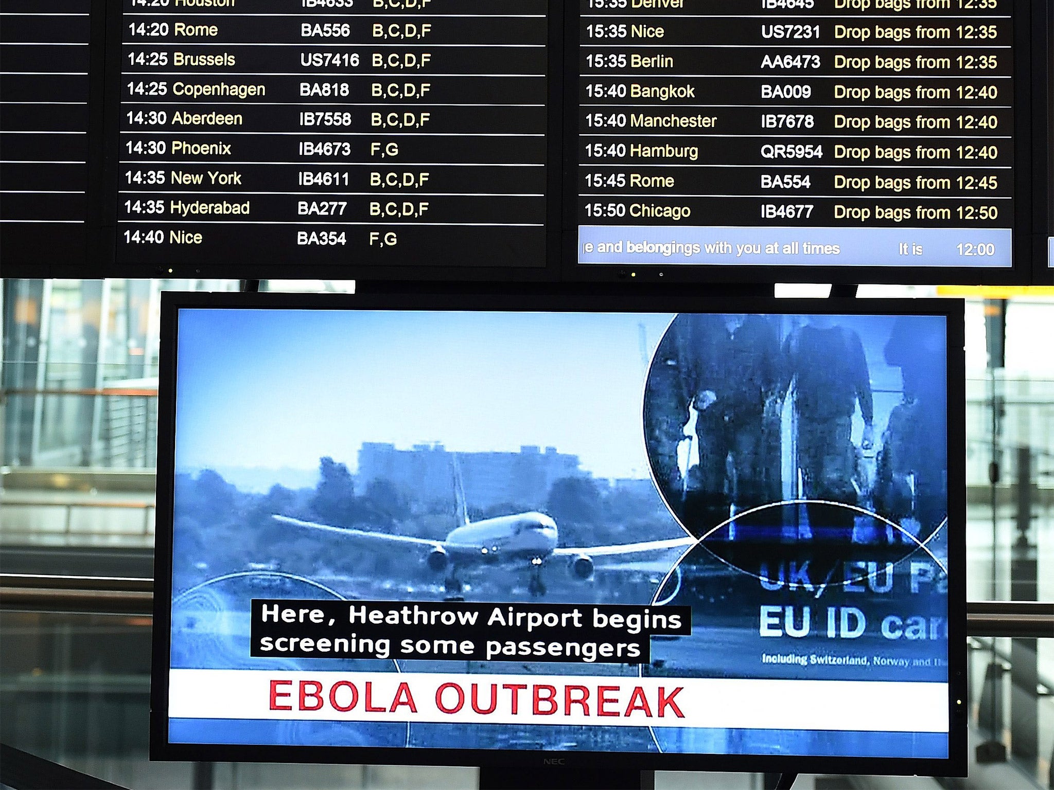 A flight information screen is shown above a television screen reporting the Ebola outbreak at Heathrow Airport