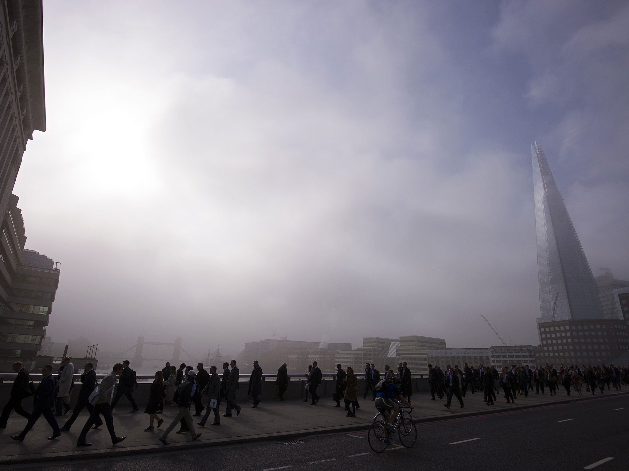 Commuters walk across London Bridge in the early morning fog in central London, on April 30, 2014.