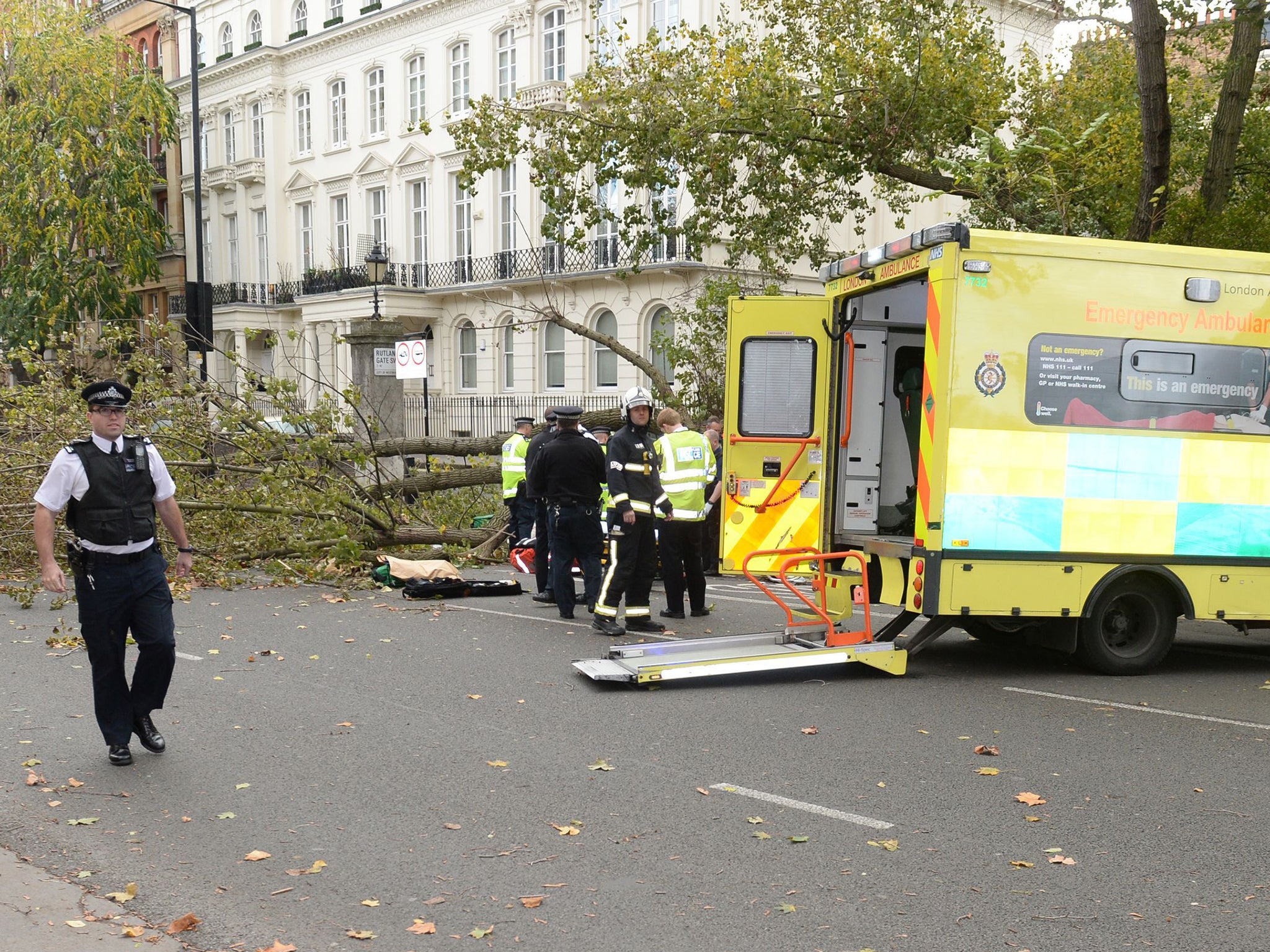 Police and London Ambulance services at the scene on Kensington Road, Kensington, west London where a woman has died after a tree fell into the street during high winds caused by the remnants of Hurricane Gonzalo