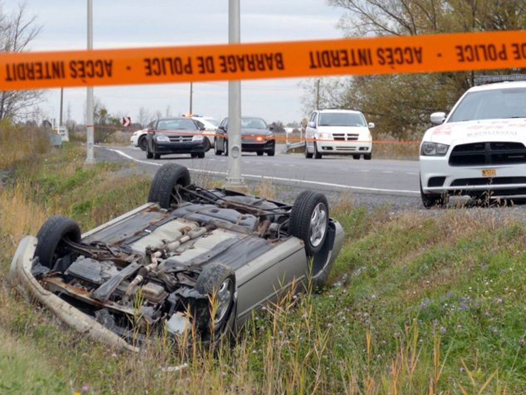 A car is overturned in the ditch in a cordoned off area in St-Jean-sur-Richelieu, Quebec on Monday Oct. 20, 2014.