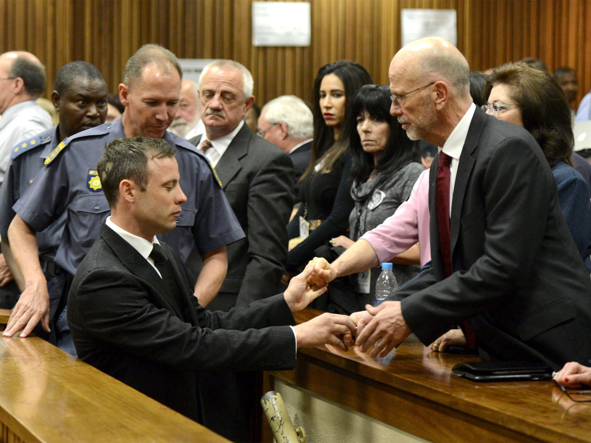 Oscar Pistorius briefly holds the hand of his uncle Arnold as he is taken to the holding cells after sentencing