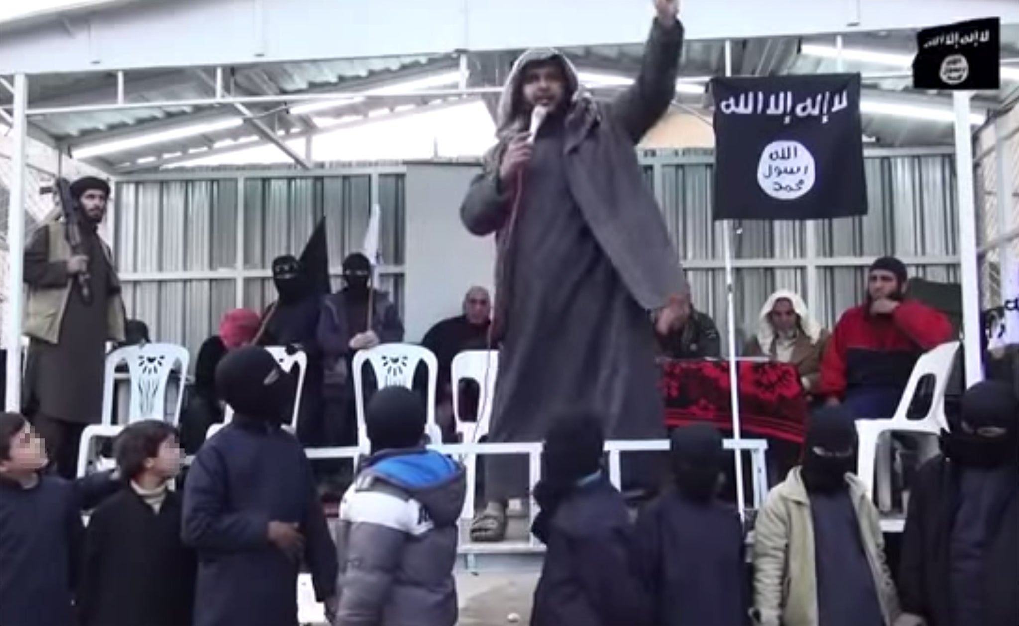 Armed men watch on as children who are thought to be 'graduating' from the Isis school stand in the foreground