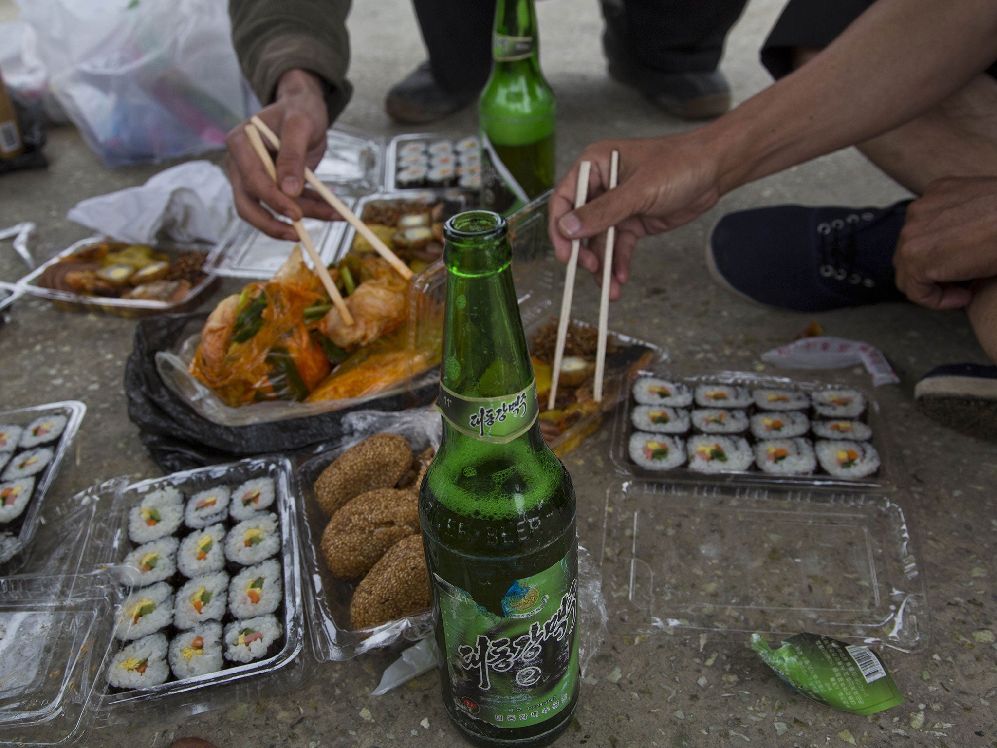 North Korean men share a picnic lunch and North Korean-brewed and bottled Taedonggang beer along the road in North Korea's North Hwanghae province.