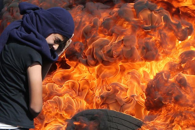 A Palestinian protester protects his face as he stands in front of burning tyres during a demonstration against the expropriation of Palestinian land by Israel in the village of Kafr Qaddum, near Nablus in the occupied West Bank