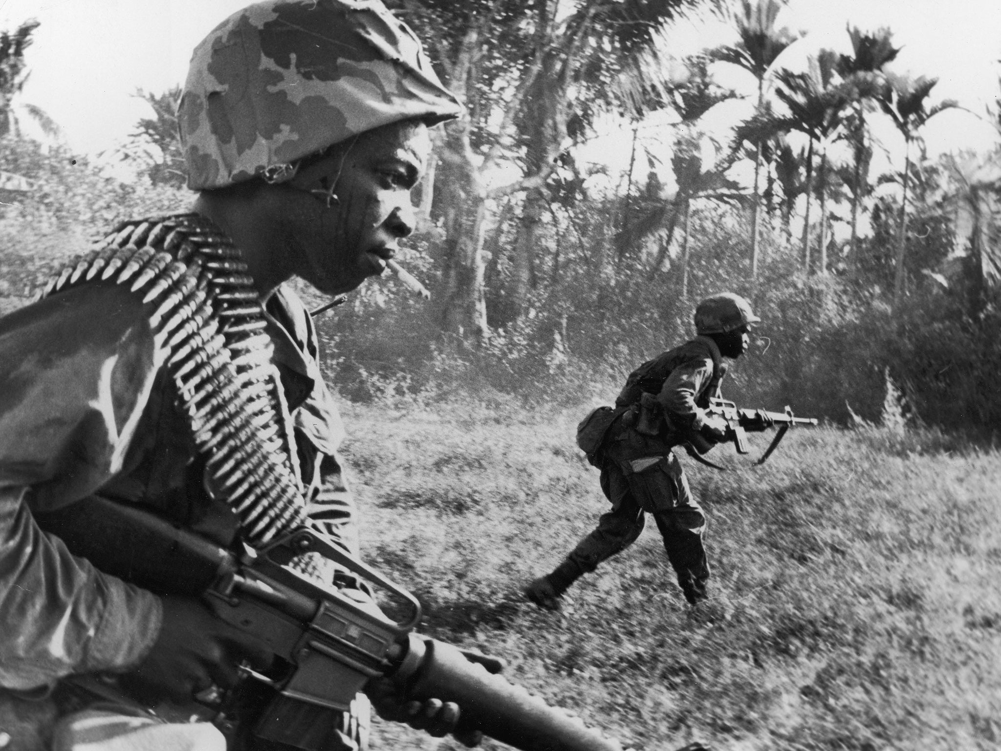 US riflemen from the 173rd Airborne Brigade charge toward Viet Cong positions, holding machine guns in a wooded area of War Zone D during the Vietnam War