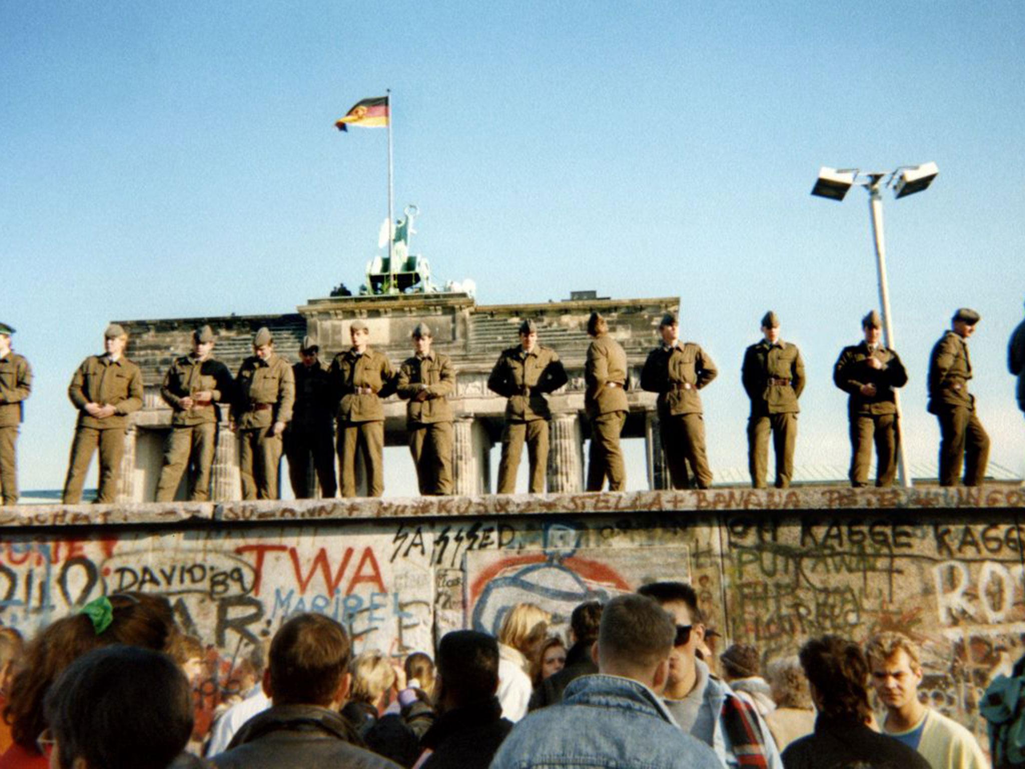 East German border guards stand on a section of the Berlin wall in front of the Brandenburg gate on November 11, 1989