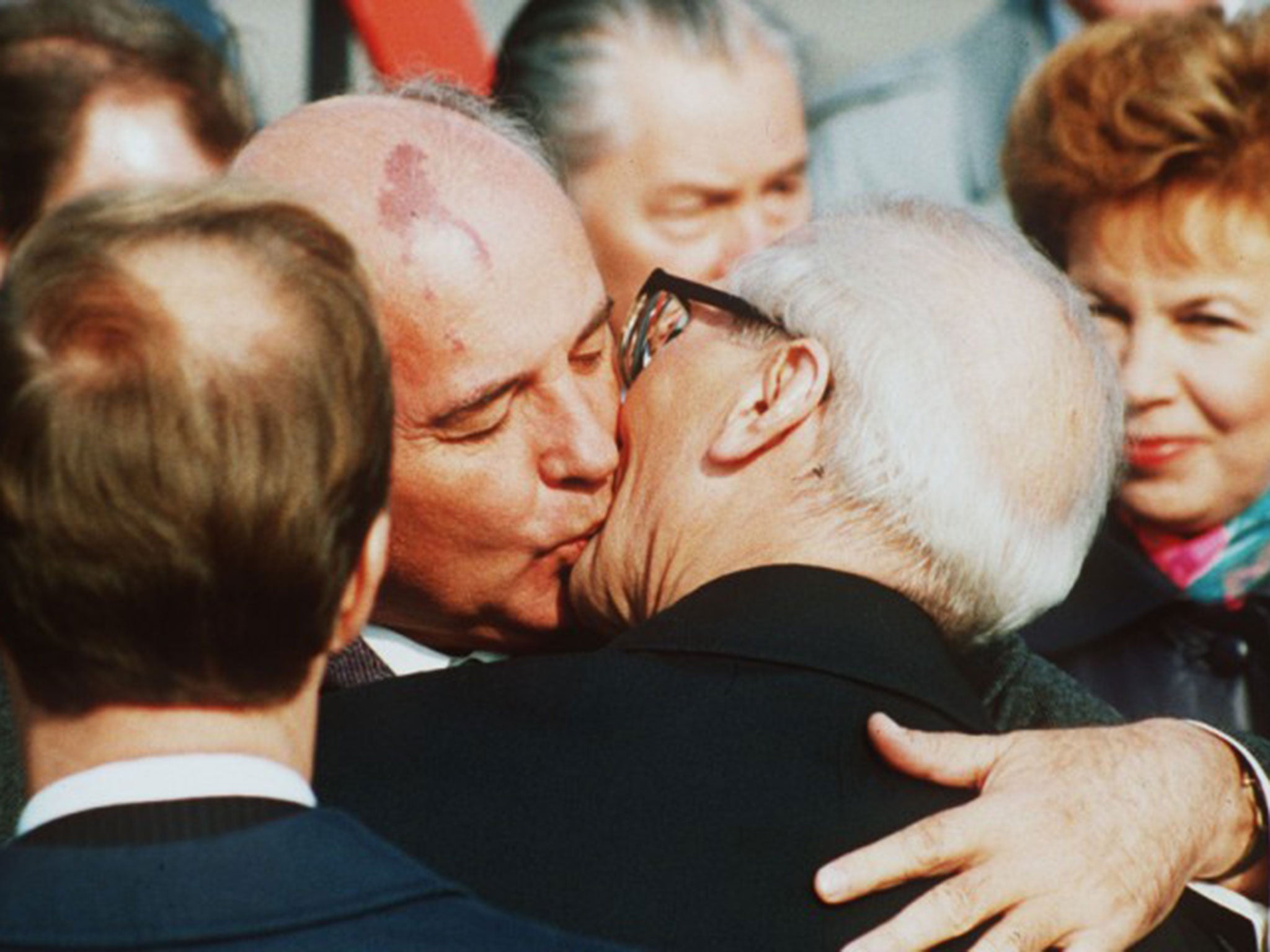 The Soviet President Mikhail Gorbachev, watched by his wife Raisa, right, kisses his East German counterpart Erich Honecker in East Berlin in October 1989