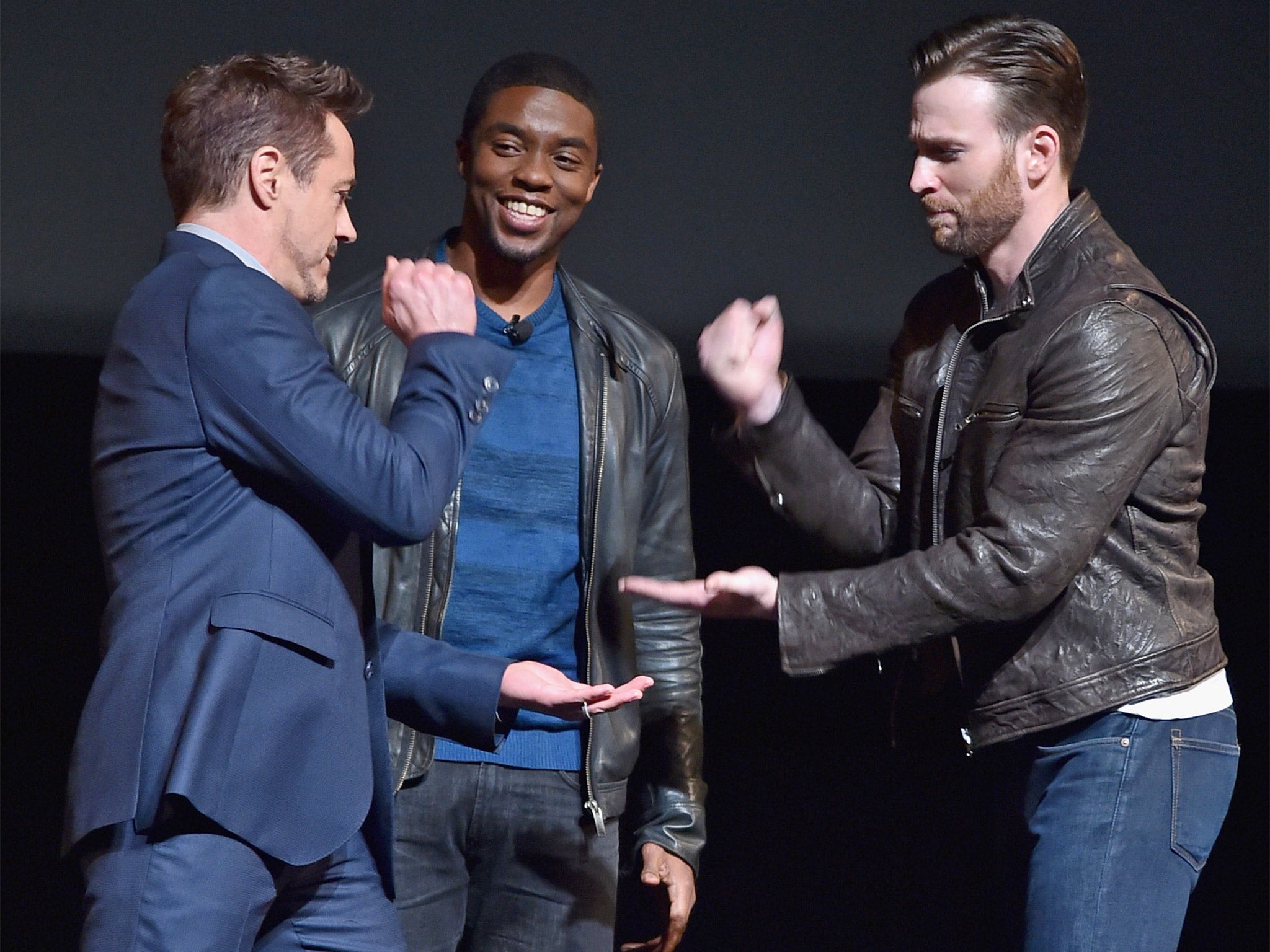 Black Panther (Boseman) looks on as Ironman (Downey Jr.) and Captain America (Evans) do battle in a game of rock-paper-scissors at a Marvel fan event in Los Angeles