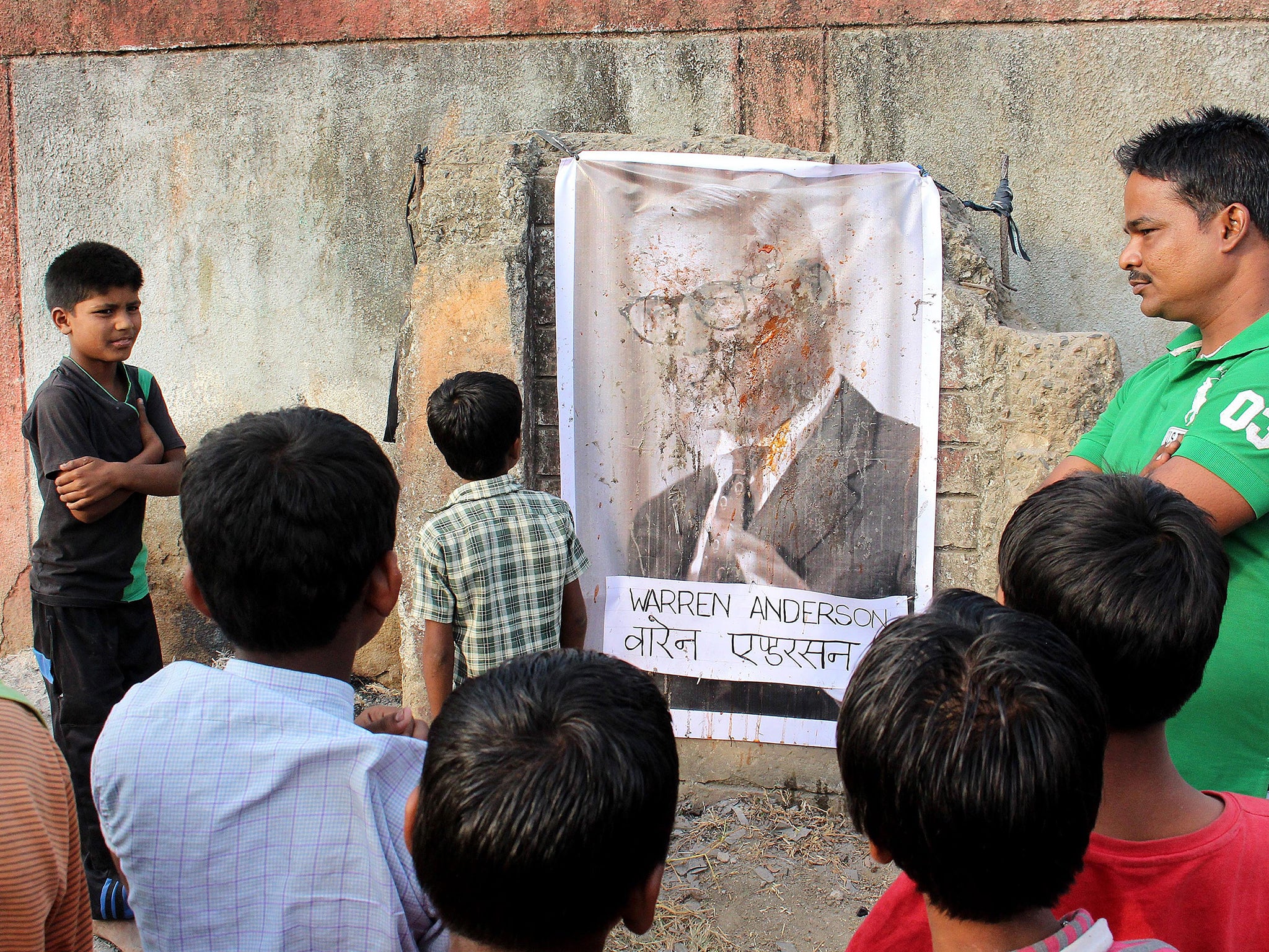 Children of gas victims looking at a defaced poster of Warren Anderson hanging on the wall of the abandoned Union Carbide plant in Bhopal after the news of his death