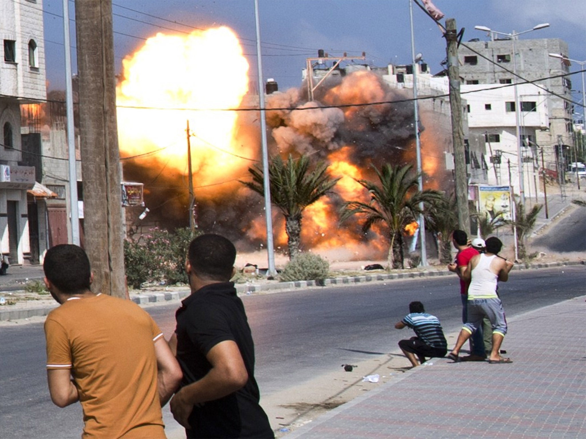 Palestinian men look on as a bomb from an Israeli air strike hits a house in Gaza City in August