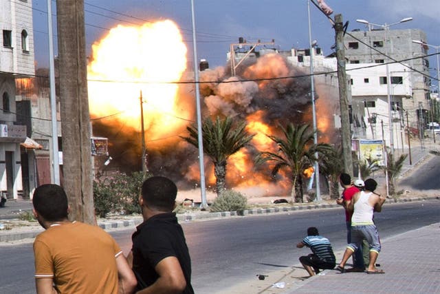 Palestinian men look on as a bomb from an Israeli air strike hits a house in Gaza City last August