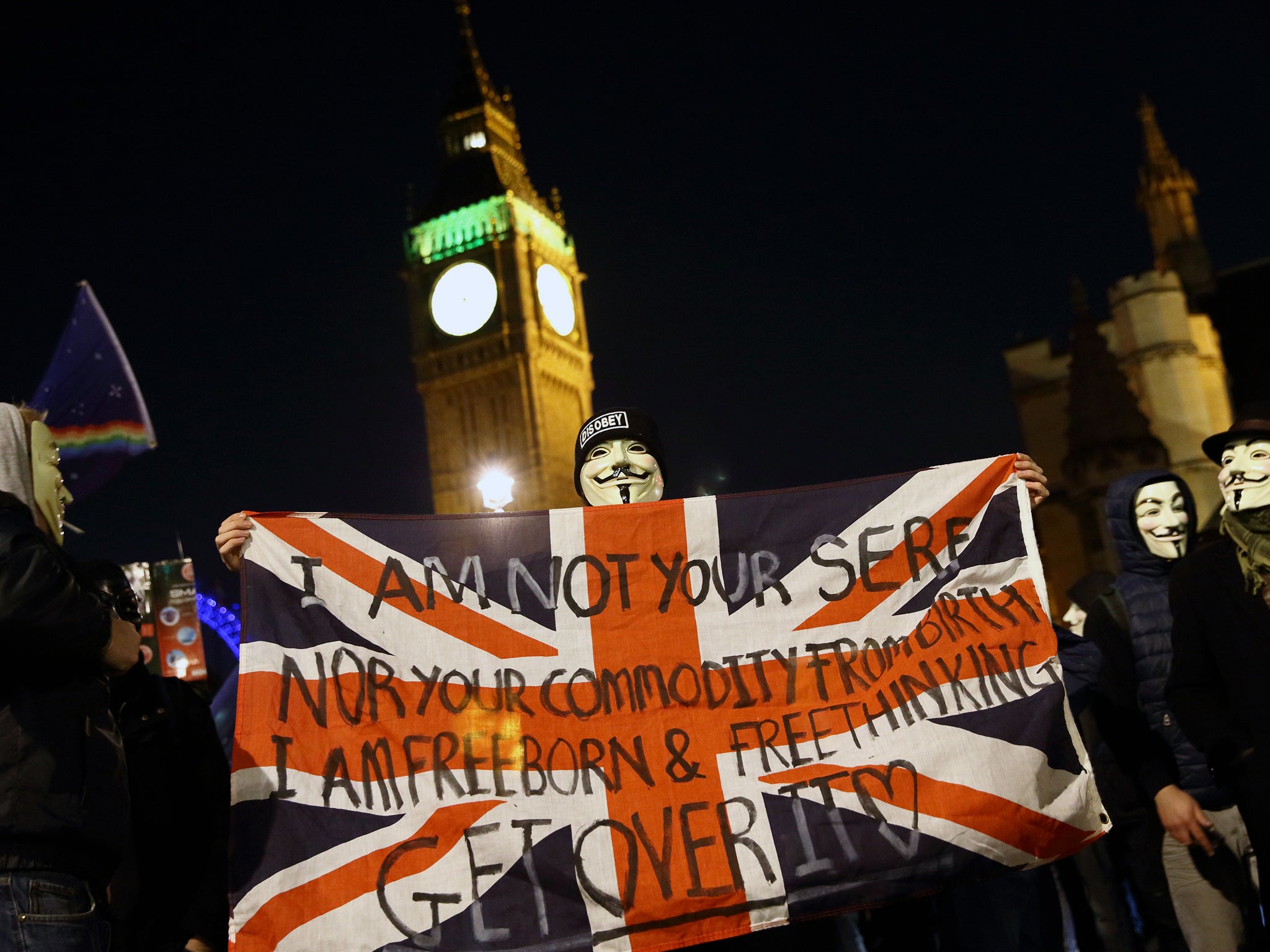 A masked protestor holds a flag outside the Houses of Parliament during the Million Mask March
