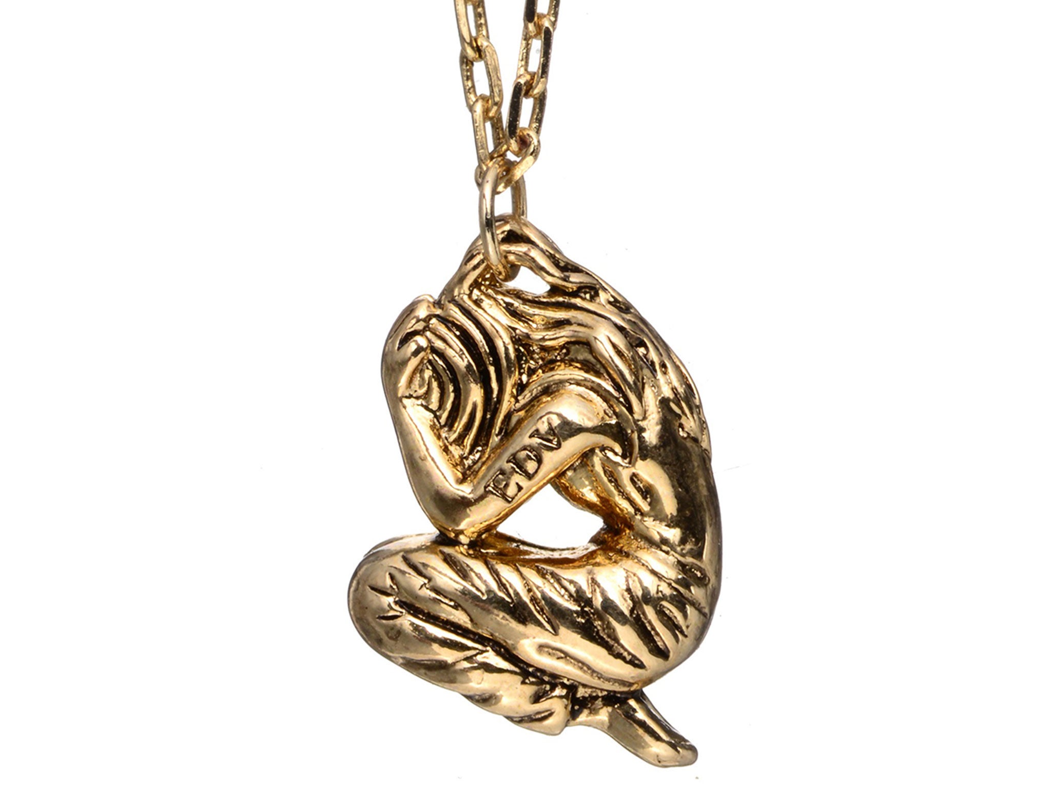 The pendant appears to be the silhouette of a woman on her knees, in fetal position, with her head in her hands