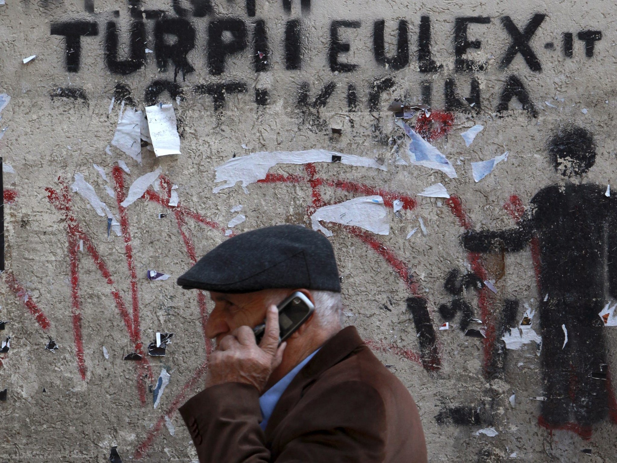 A man passes by a wall with graffiti which reads "The shame of EULEX" in Pristina