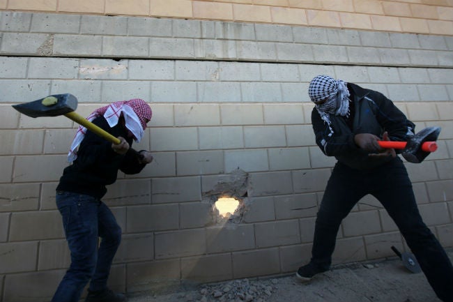 Palestinian activists knocking a hole into the brick barrier yesterday